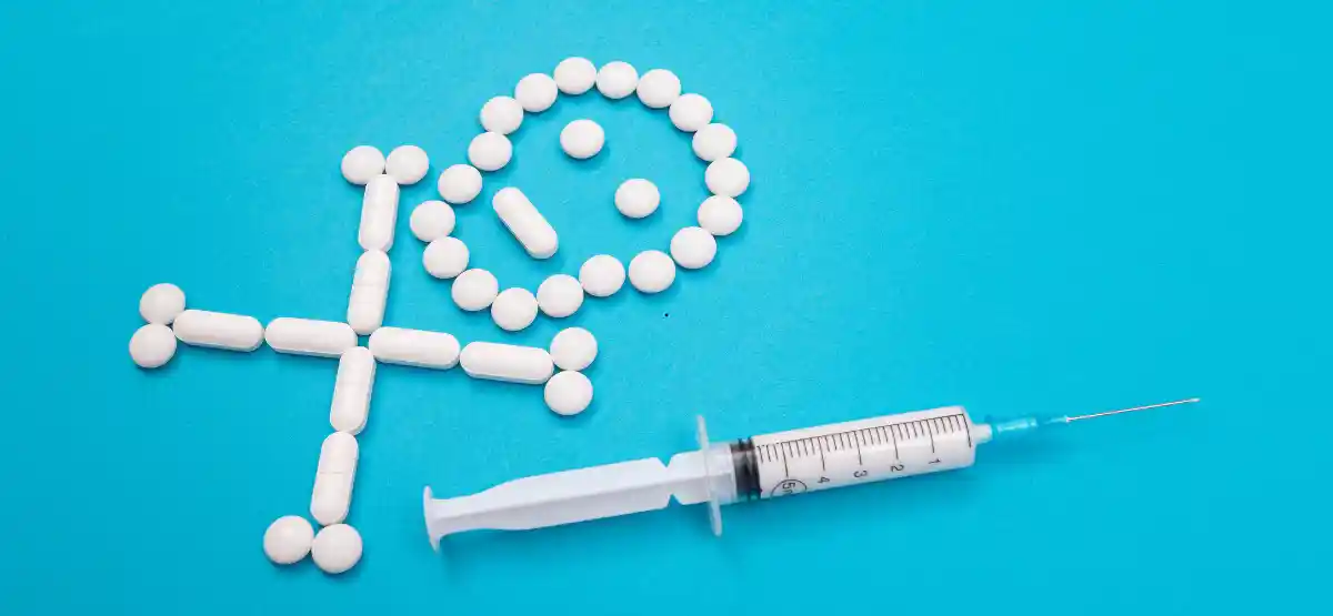 White tablets arranged to form a skull and crossbones on a blue background, with a syringe placed next to the symbol.