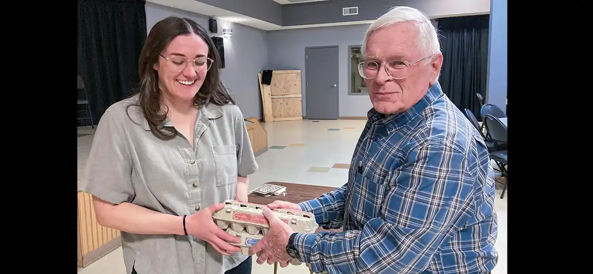 Kennedy Halvorson smiles while receiving a carton of fresh eggs from Allan Garbutt after her Crowsnest Conservation Society presentation.